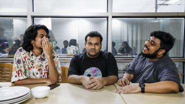A man with a poker face sitting with two laughing friends.